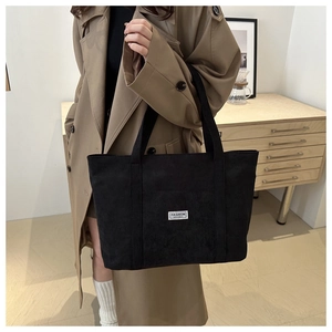 Close-up of black corduroy tote bag featuring a white Fashion Instinct label detail