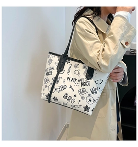 Detail of white leather tote bag featuring artistic black graffiti prints and black shoulder strap