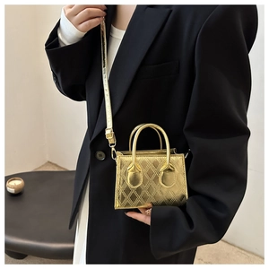 Dettaglio mini borsa dorata trapuntata con manici e tracolla su uno sfondo di blazer nero