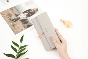 Close-up of light grey long leather wallet with leaf pendant and golden text details