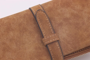 Detail of brown suede long wallet featuring white contrast stitching and zip closure