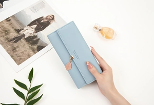 Close-up of light blue trifold leather wallet featuring a decorative metal leaf pendant