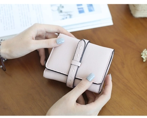 Close-up of pink short wallet with vertical stitched buckle held in hand over wooden desk