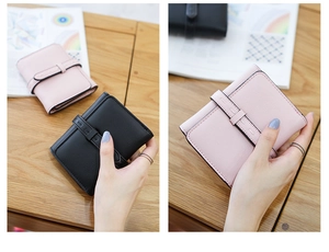 Close-up of stylish pink and black women's leather wallets with buckle on wood desk