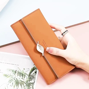 Detail of tan faux leather long wallet featuring a decorative gold leaf pendant clasp