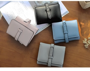 Short leather wallets for women in four pastel colors with metal buckle on wood surface