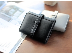 Detail of short leather wallets with buckle closure and pebbled texture on wood desk