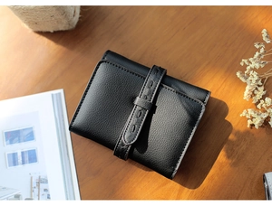 Close-up of black litchi grain leather wallet with belt buckle on a wooden desk