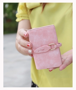 Pink matte leather card holder with gold D-ring buckle held in hand outdoors