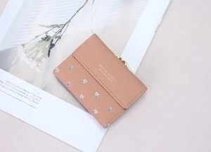 Detail of dusty pink floral wallet with gold metal clasp on botanical magazine