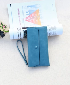 Close-up of matte teal long wallet with snap button and wrist strap on a magazine