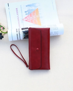 Detailed view of long red leather wallet featuring a snap button and wristlet strap