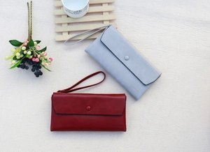 Top view of long leather wallets in grey and wine red with wrist straps and logo detail