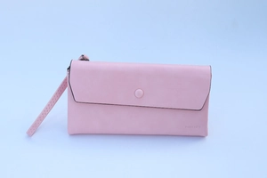 Detail of pink long wallet with wrist strap, matte texture and circular snap closure