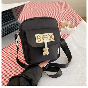 Detail of black canvas shoulder bag with BOX patch and yellow bear charm ornament