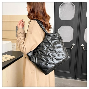 Gros plan d'un grand sac cabas noir matelassé porté avec un trench-coat marron clair
