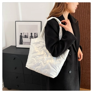 Borsa tote trapuntata bianca lucida indossata su un cappotto nero per uno stile da ufficio