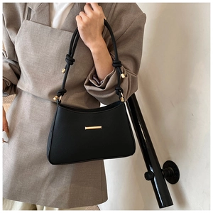 Detail of black leather underarm bag with gold buckle and knotted strap on gray blazer