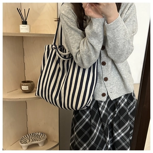 Minimalist blue and white striped canvas tote bag worn by a model in a cozy indoor setting