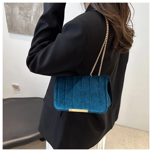 Detail of dark teal velvet shoulder bag with gold chain strap and elegant vertical quilting