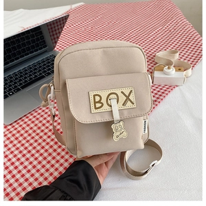 Detail view of beige canvas crossbody phone bag with cute bear charm and box patch