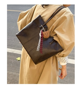 Detail of dark brown oil wax leather tote bag with plush bear charm on model shoulder