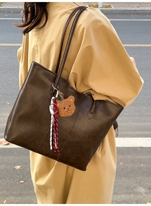 Detail of deep brown leather tote bag with a cute plush bear charm and woven rope accent