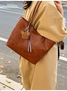 Close-up of brown vintage tote bag with plush bear charm and striped ribbon detail