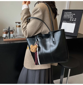 Minimalist black tote bag with plush bear charm shown in a stylish side view on model