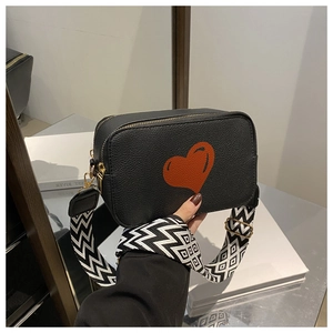 Detail of black pebbled leather crossbody bag featuring a red heart and geometric strap