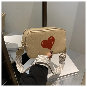 Detail of beige lychee leather crossbody bag with red heart and woven strap
