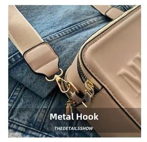 Close-up of golden hardware hook and embossed letter M on beige leather crossbody bag