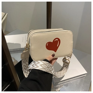 Detail of beige crossbody bag featuring a large red heart and woven geometric strap