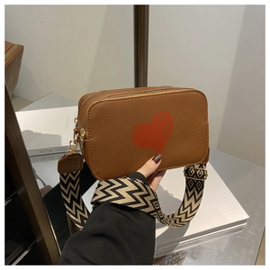 Detail of brown leather crossbody bag featuring red heart and geometric wide strap