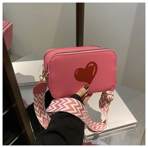 Detail of pink leather crossbody bag with red heart pattern and geometric woven strap