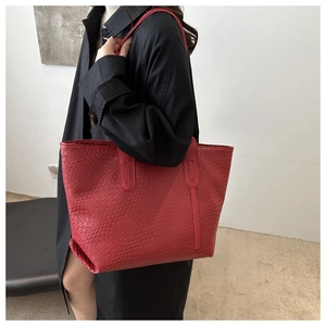 Close-up of a large red woven tote bag with Intrecciato texture worn on the shoulder