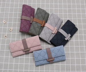 Multiple colors of long tri-fold wallets featuring clover embossed pattern and strap buckle