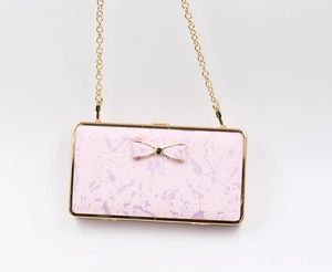 Pink marble clutch bag with gold bow detail and metallic chain strap on white background