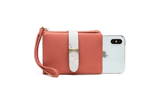 Close-up of coral pink wallet with floral band and wrist strap next to a phone for scale