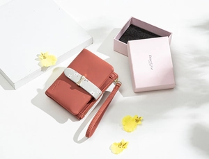 Close-up of coral pink leather wallet with floral strap, metal bow, and wristlet detail