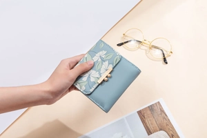 Close-up of a floral print tri-fold wallet with a gold metallic engraved snap closure