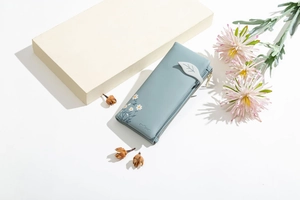 Detail of blue faux leather wallet with daisy print and leaf buckle on flat lay background