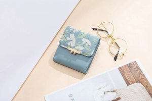 Detail of light blue floral print tri-fold wallet with gold bead clasp and metal logo plate