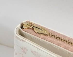 Detail of leaf-shaped gold zipper pull on floral print cream faux leather wallet