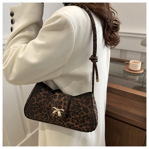 Detail of leopard print underarm bag featuring a golden metal bow buckle and knotted strap