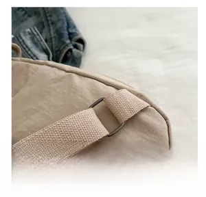 Close-up of durable metal buckle and reinforced strap on a beige nylon crossbody bag