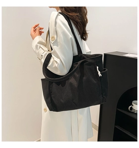 Detail of black corduroy tote bag showing textured vertical stripes and side drawstring