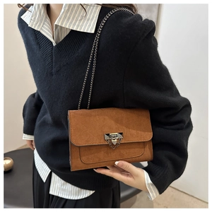 Sac bandoulière en daim marron avec chaîne métallique porté à l'épaule par un mannequin
