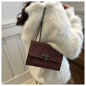 Détail d'un sac en daim bordeaux avec chaîne porté sur un pull en peluche blanc chic