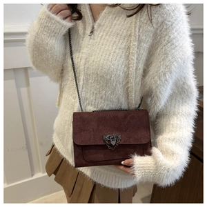 Détail du sac à rabat en daim bordeaux avec chaîne métallique et fermoir sur modèle
